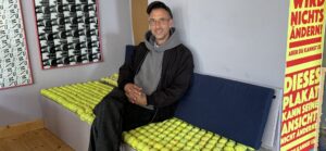 Jan Schlake sitzt lächelnd auf Bänken mit Tennisball-Polsterung. Blick ins Café Courage in Döbeln.