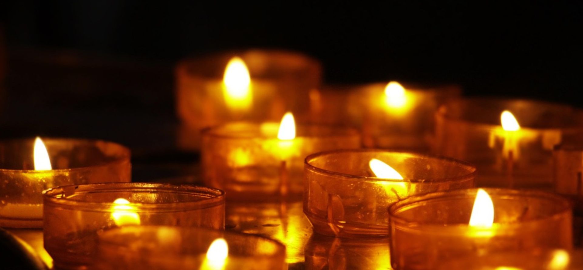 Zusehen sind Teelichter in Glässer die Brennen. Der Hintergrund ist Schwarz weil es beretis Abend ist. Diese Teelichter sind bestandteil der Mahnwachen an den Stolpersteinen.