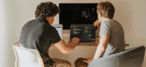 Zwei Personen sitzen vor einem Computer und programmieren zusammen.