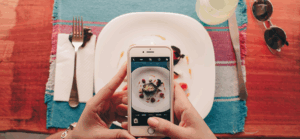 zwei Hände halten ein Smartphone über einen Teller mit Essen, um ein Foto zu machen
