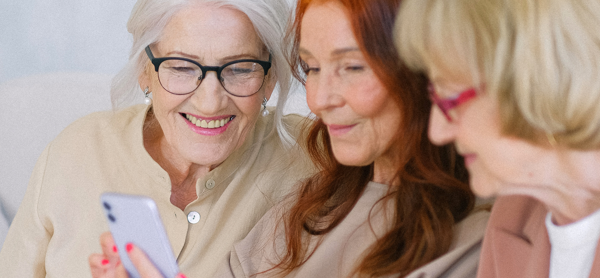 drei ältere Damen sehen zusammen auf ein Smartphone